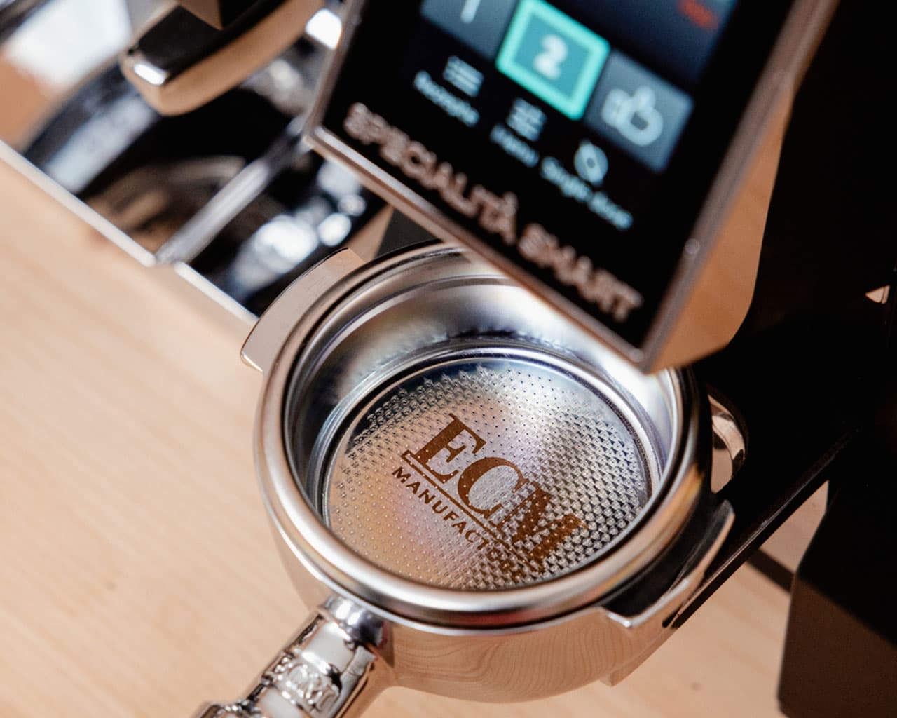 Nahaufnahme Siebträger mit ECM-Logo in einer ECM Estetika Espressomaschine, Bildschirm und Metalloberflächen sichtbar