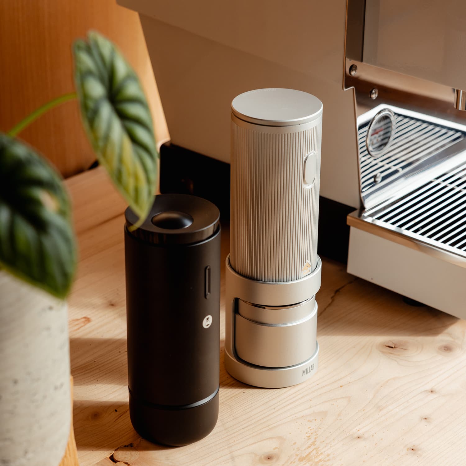 Zwei portable Timemore Kaffeemühlen (silber Millab E01 und schwarz Whirly 01S) neben Siebträgermaschine auf Holz