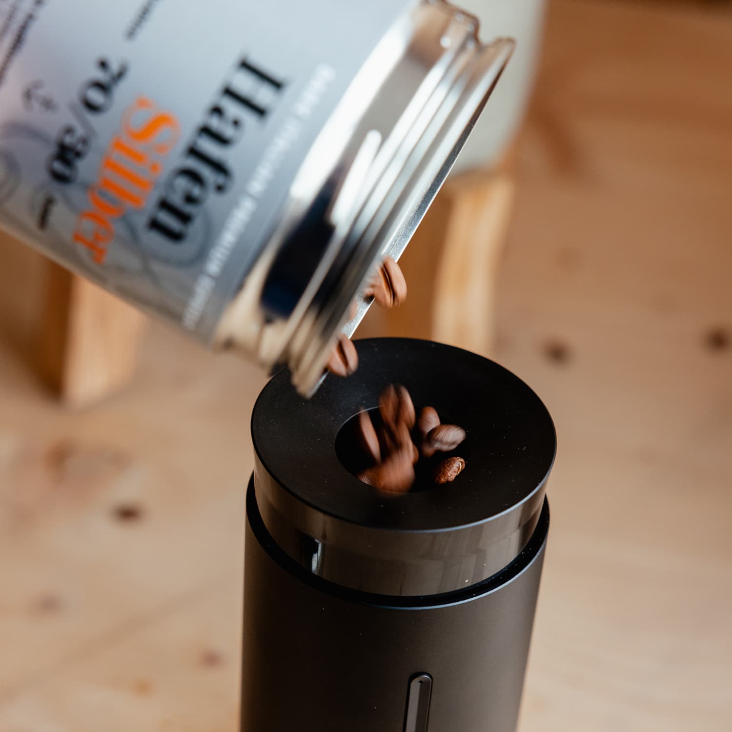 Kaffeebohnen werden aus einer Dose in die Öffnung einer schwarzen Timemore Handmühle geschüttet