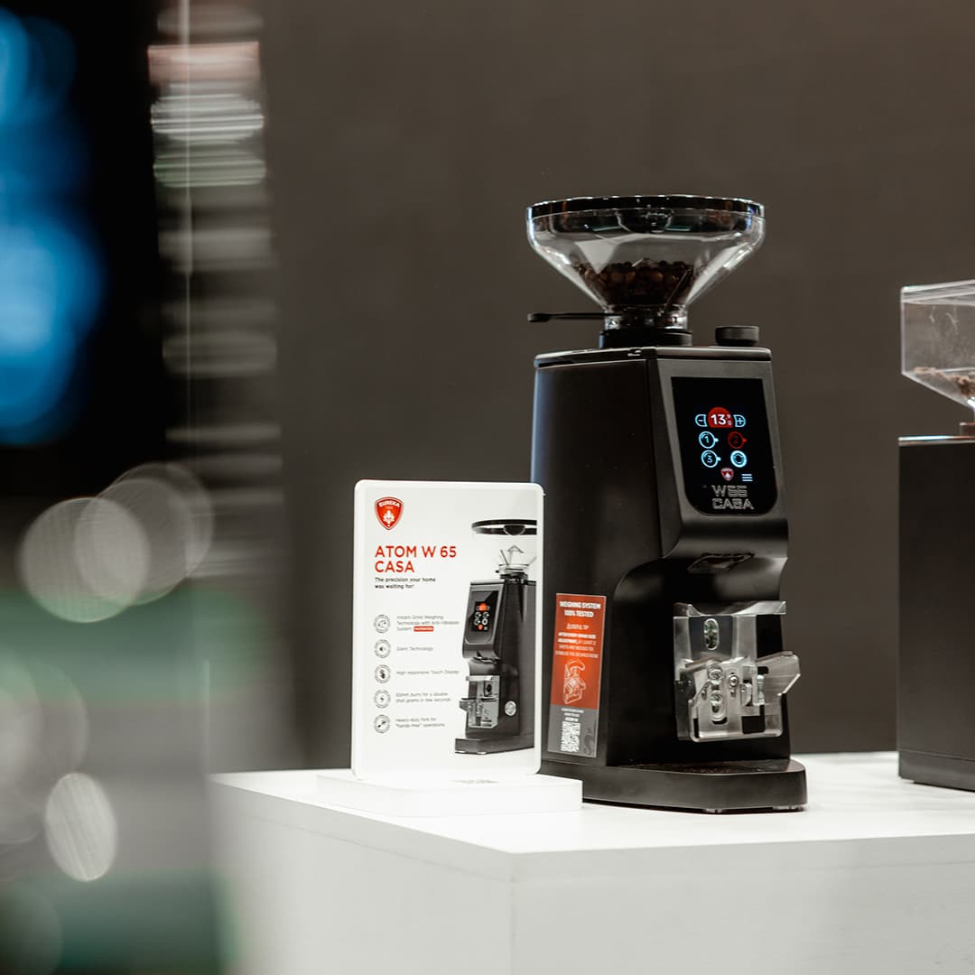 Schwarze Eureka Kaffeemühle Atom W 65 Casa mit Bohnenbehälter und Display auf Messestand (Host Milano 2025)