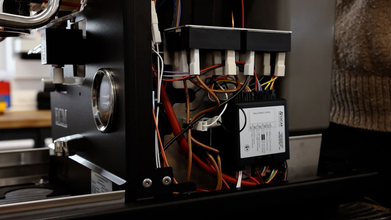Offenes Gehäuse einer ECM Estetika Siebträgermaschine mit sichtbaren Kabeln, Elektronikmodul und Manometer in der Werkstatt