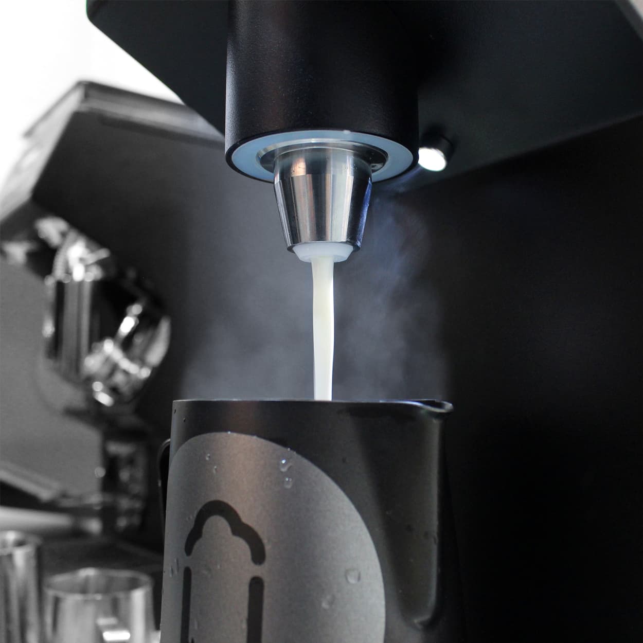 Milchstrahl aus Dampfdüse füllt schwarzes Milchkanne, Dampf sichtbar, Übermilk Espresso-Zubehör