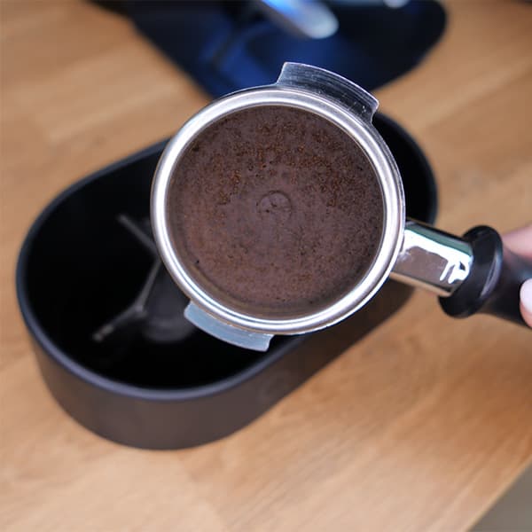 Portafilter mit frisch getamptem Kaffeemehl über schwarzem Auffangbehälter auf Holzarbeitsfläche