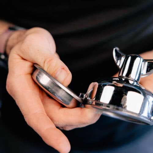 Hand hält Edelstahl-Siebträger und Tamper einer Espressomaschine, Nahaufnahme für Heim-Espresso-Zubereitung