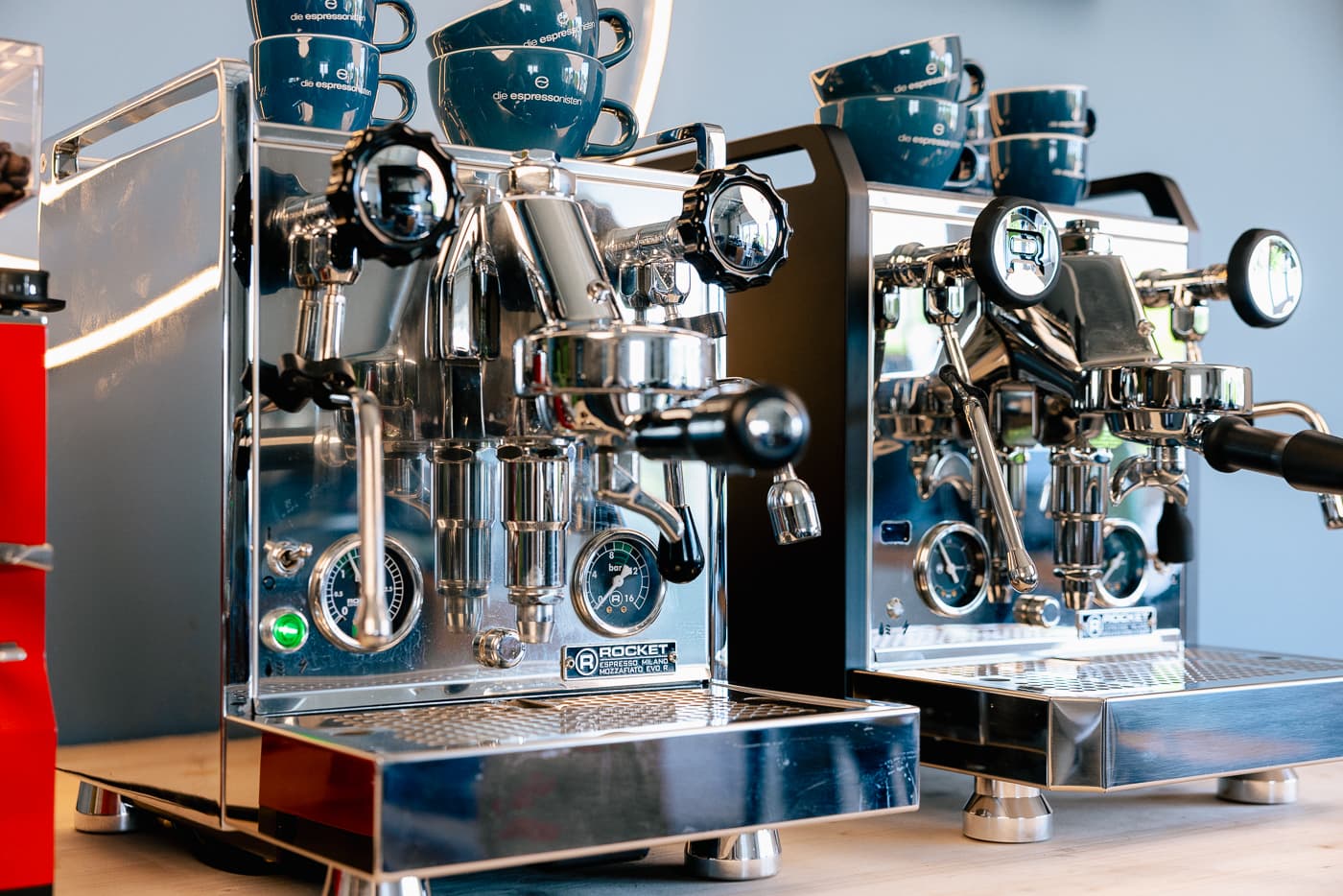 Zwei glänzende Rocket Mozzafiato Cronometro V Fast Espressomaschinen mit Siebträgern, Manometern und blauen Tassen auf der Ablage